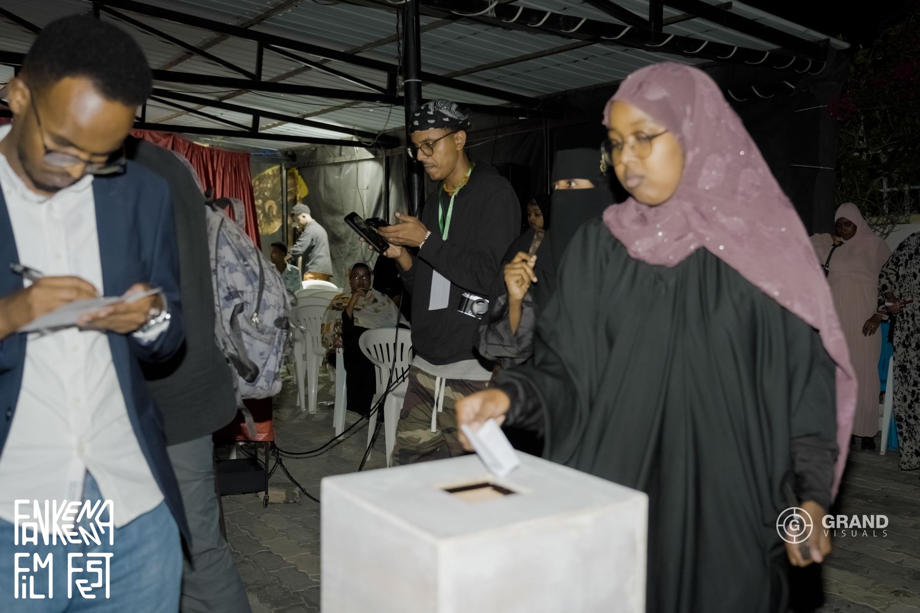 A visitor puts her vote in the ballot box while others fill in their cards