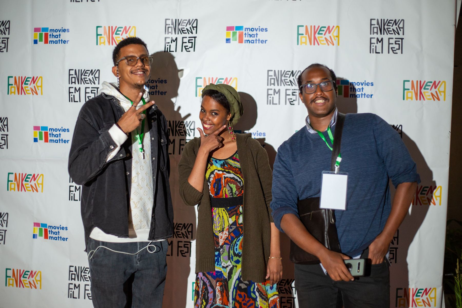 Three guests pose in front of the festival wall